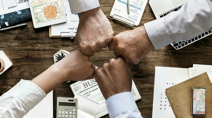 Starke Partnerschaften bei onmaps – Zusammenarbeit auf Augenhöhe für gemeinsame Erfolge Vier Geschäftspartner stoßen mit Fäusten über einem Schreibtisch zusammen – Symbol für Teamwork, Vertrauen und erfolgreiche Partnerschaft bei onmaps, mit Karten und Geschäftsunterlagen im Hintergrund.